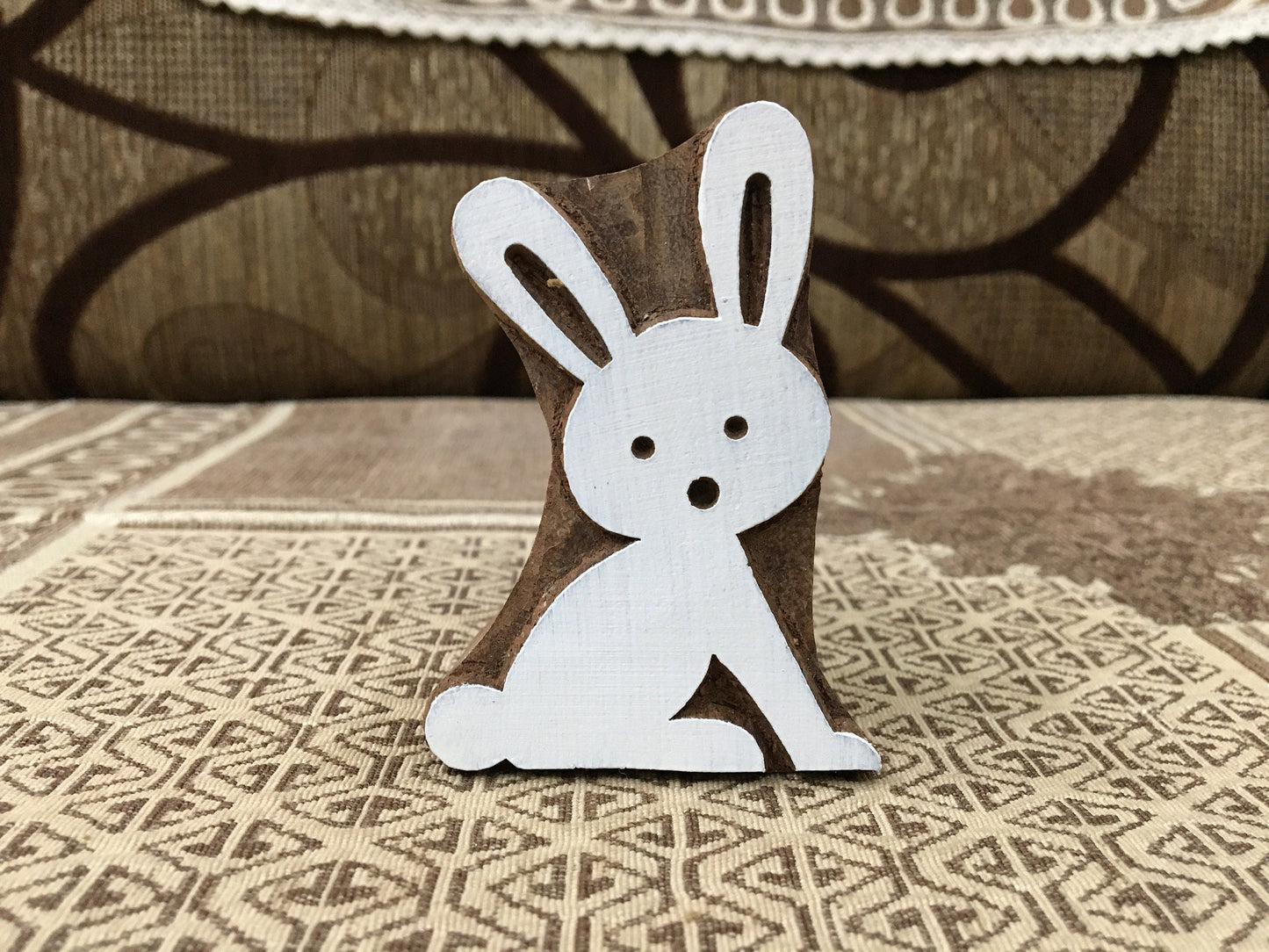 Wooden rabbit figurine on a textured surface with a patterned rug in the background