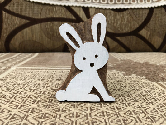 Wooden rabbit figurine on a textured surface with a patterned rug in the background